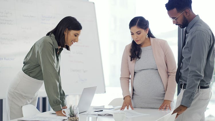 A pregnant employee and two colleagues review documents together at a conference table